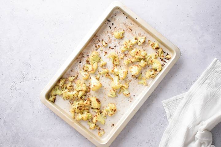 Roasted cauliflower on a white baking sheet.