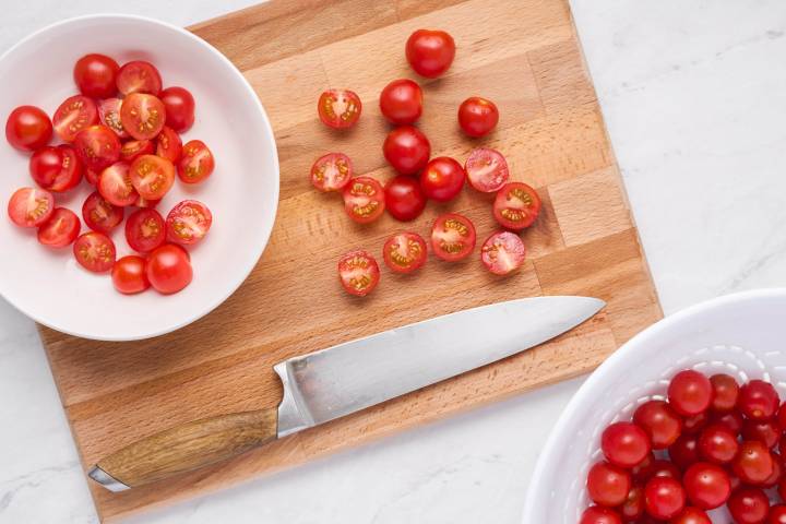 Cutting board with grape tomatoes cut in half and a knife.