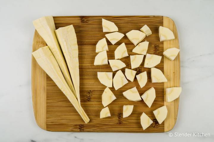 Parsnips peeled and cut into quarters on a wooden cutting board.