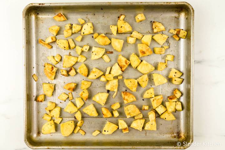 Roasted parsnips in a baking sheet with salt, pepper, and spices.