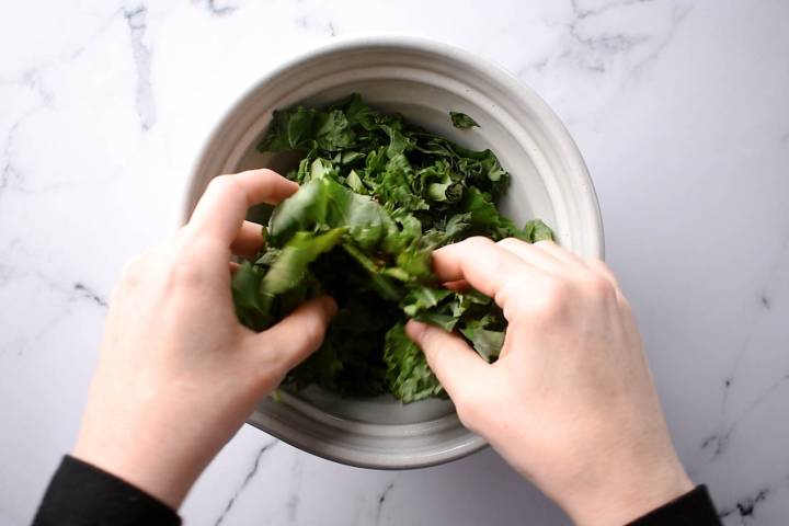Kale being massaged with a maple Dijon vinaigrette dressing.