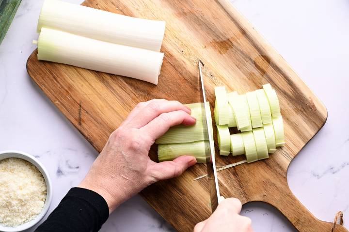 Leeks being sliced into 1/2 inch pieces on a cutting board.