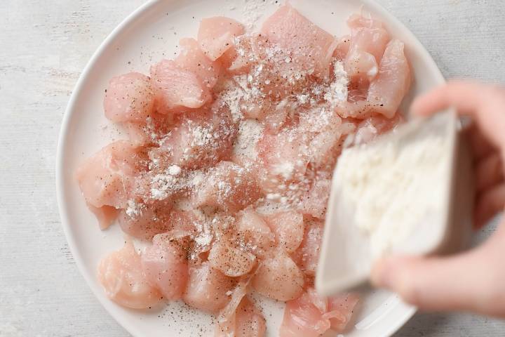 Chicken breast being tossed with salt, pepper, and flour.
