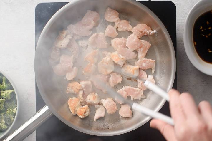 Chicken breast chunks being browned in a pan.