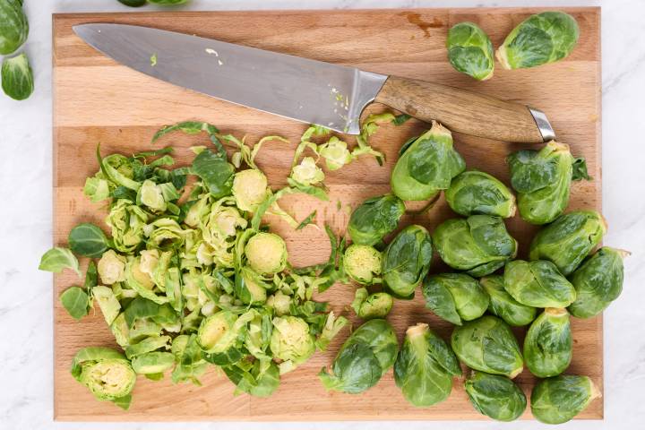 Shredded and whole Brussels sprouts on a cutting board with a knife.