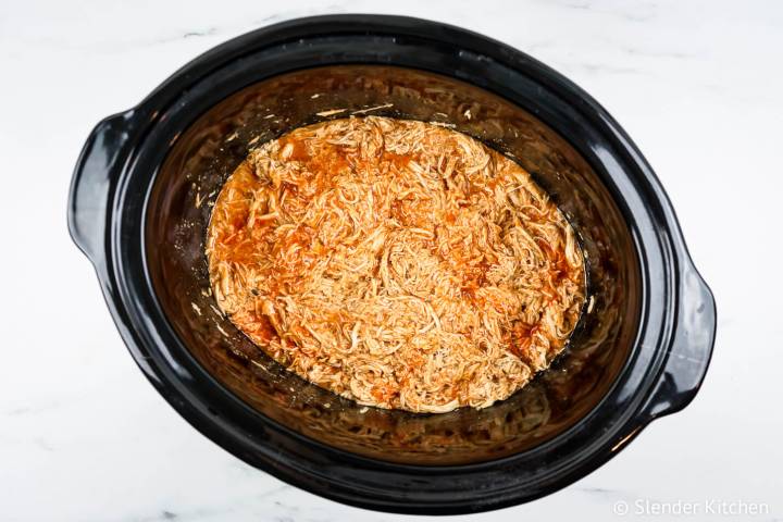 Shredded buffalo chicken in a black slow cooker.