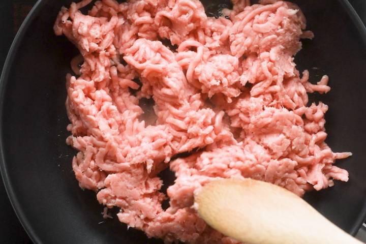 Ground chicken in a skillet with a wooden spoon.