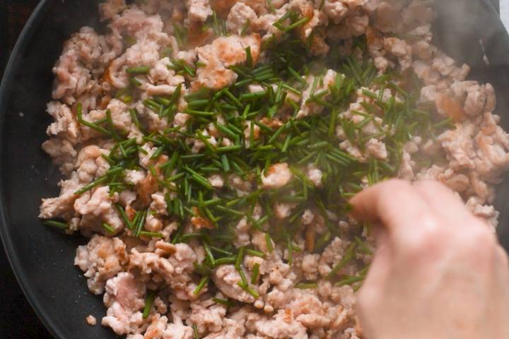 Green onions, garlic, and ginger being added to ground chicken in a skillet.