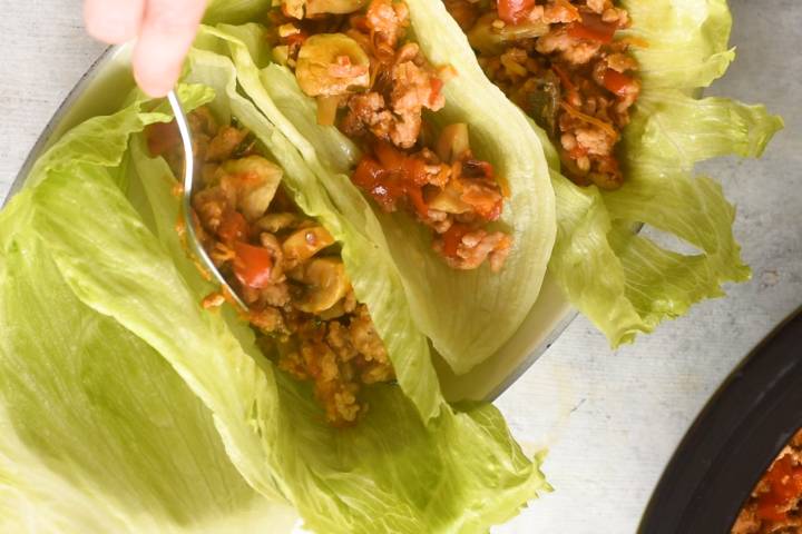 Chicken lettuce wraps being assembled with lettuce leaves and ground chicken.