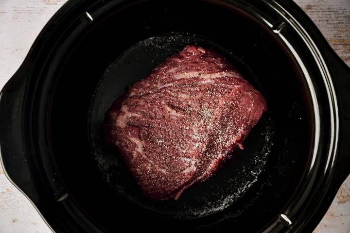 A seasoned beef roast sits in a slow cooker, ready to be cooked low and slow for a tender and flavorful Mexican beef adobo.