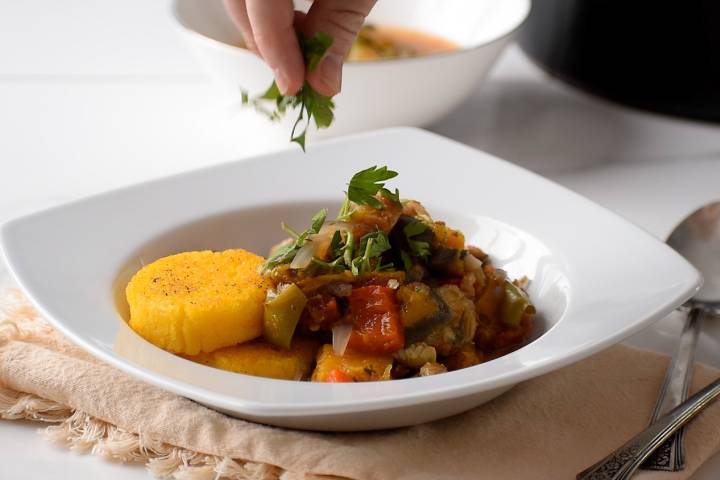 Ratatouille in a bowl being topped with fresh herbs and vinegar.