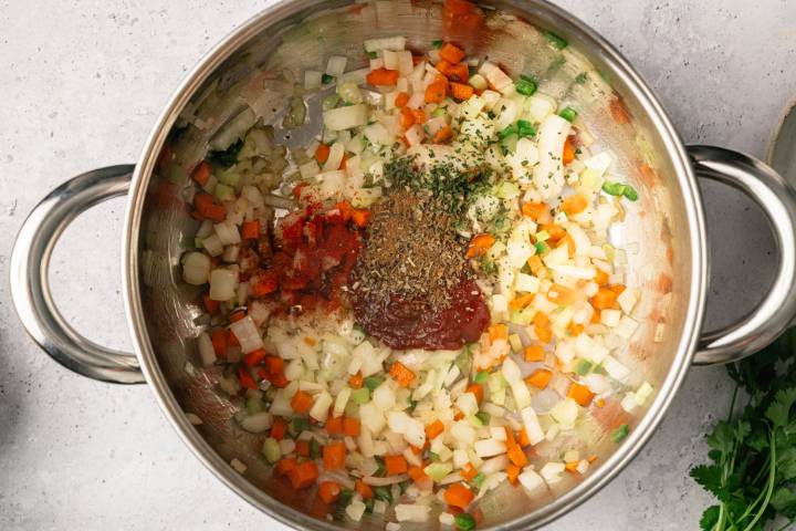 Chopped onions, carrots, and celery in a pot with tomato paste and herbs, ready to cook. Fresh parsley on the side. Bright, fresh, and inviting.