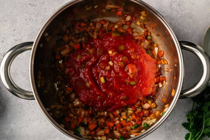 A stainless steel pot filled with sautéed onions, carrots, and zucchini, topped with a vibrant red tomato sauce on a light countertop, creating a fresh, wholesome vibe.