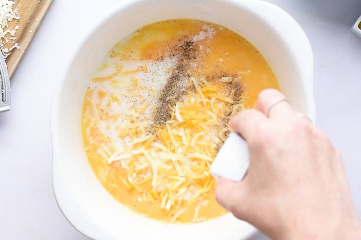 Eggs, milk, and cheese in a bowl with a whisk.