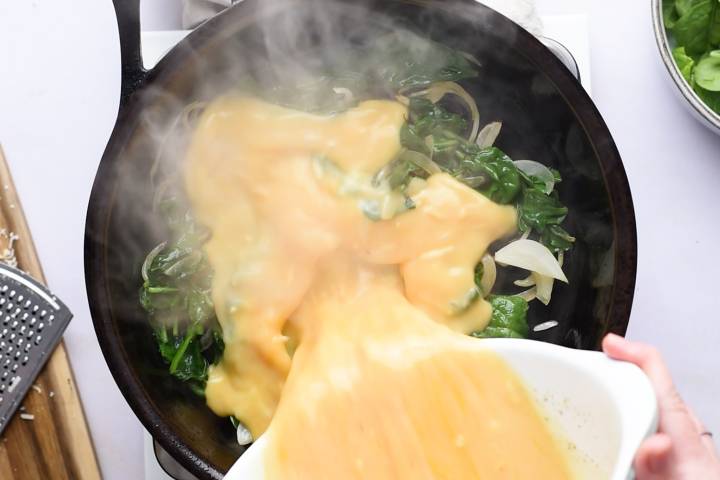 Egg mixture being poured into a skillet with spinach.