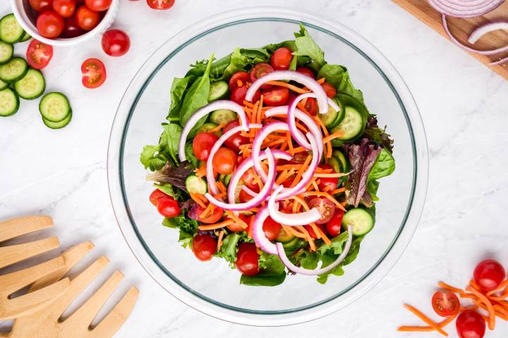 Spring mix with tomatoes, carrots, red onions, and cucumbers, in a bowl.