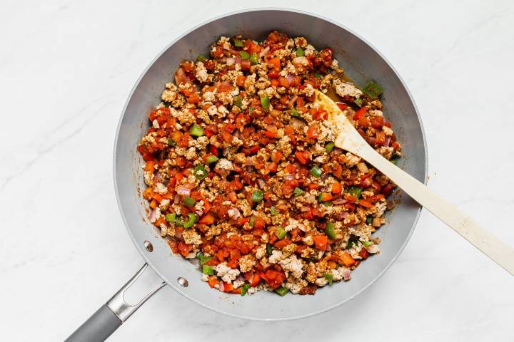 Ground turkey with peppers, onions, and tomatoes in a skillet with fajita seasoning.