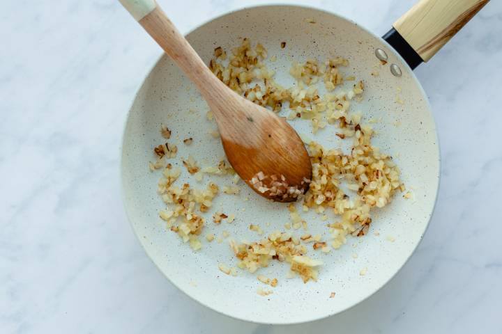 Onions being cooked in olive oil in a skillet.