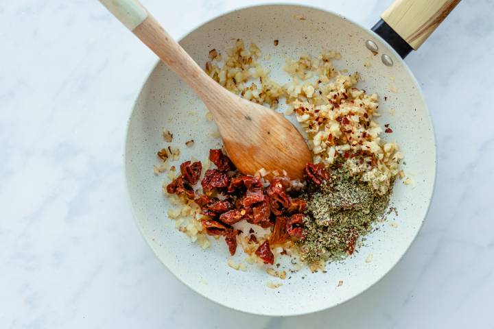 Sundried tomatoes, garlic, and spices being cooked in a skillet.