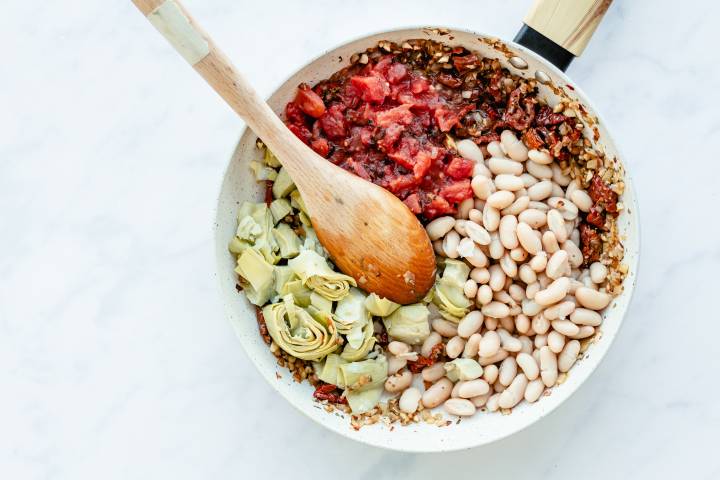 White beans, diced tomatoes, and artichoke hearts in a skillet.