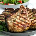 Healthy grilled pork chops on a plate with fresh herbs and salad.