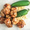 Barbecue cheddar meatballs on a cutting board with fresh jalapenos on the side.