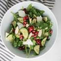 Arugula, cucumber, and pomegranate salad in a bowl with shaved Parmesan cheese.