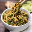 Asian zucchini noodles in a bowl with chopsticks lifting out a spoonful.