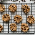 Banana chocolate oat cookies on a wire rack with bananas and dark chocolate chips on the side.