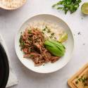 Beef machaca served with white rice in a bowl with cilantro and avocado on top.