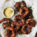 Grilled shrimp garnished with herbs, served with a creamy dipping sauce on parchment paper, ready to enjoy.