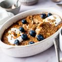Cinnamon baked oatmeal with rolled oats baked in a white dish topped with blueberries and honey.