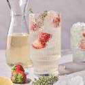 A tall glass of white wine spritzer garnished with strawberries and thyme sits next to a carafe of wine.