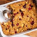 Golden-baked oatmeal casserole with cranberry and apple chunks in a white dish. 