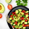 Cucumber avocado salad with tomatoes in a wooden bowl.