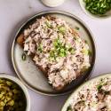 A top-down shot of an open-faced dill pickle tuna salad sandwich, with bowls of the salad, pickles, and green onions on the side.