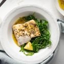 Easy baked cod with a lemon, garlic, and butter sauce on a white plate with mixed greens.