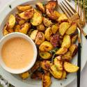 Easy roasted potatoes coated in olive oil and mustard on a white plate with dipping sauce and herbs.