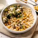 A bowl of roasted broccoli, chickpeas, and grains topped with a creamy sauce. 