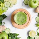 Green juice made with cucumbers, celery, kale, spinach, green apples, ginger, and lime juice in a glass.