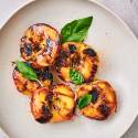 Grilled peaches with dark brown grill marks served on a plate with honey and fresh basil.
