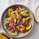 A colorful medley of roasted zucchini, yellow squash, cherry tomatoes, and red onion served with lemon on a light table setting.
