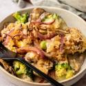 A bowl of broccoli and mushroom casserole topped with crispy breadcrumbs and caramelized onions. A fork rests on the bowl, adding a cozy, inviting feel.