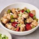 A bowl of Healthy Kung Pao Chicken featuring chunks of chicken, red bell peppers, celery, and garnished with green onions and peanuts.