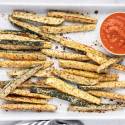 Low carb Parmesan zucchini fries with crispy edges served on a baking sheet with marinara sauce.