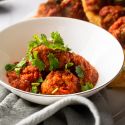 Mexican chipotle meatballs in a spicy tomato sauce in a bowl with chopped cilantro and corn tortillas.