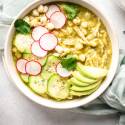 Green chicken pozole in a bowl with avocado, radish, cilantro, chicken, and hominy.