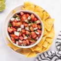 Pico de gallo with diced tomatoes, white onion, cilantro, jalapeno, and lime juice in a white bowl with tortilla chips on the side.