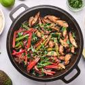 Pork fajitas with thin strips of pork, bell peppers, onion, cilantro, and limes in a cast iron skillet.