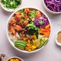 Salmon poke bowls with raw salmon, white rice, avocado, green onions, cucumber, seaweed, edamame, and cabbage.